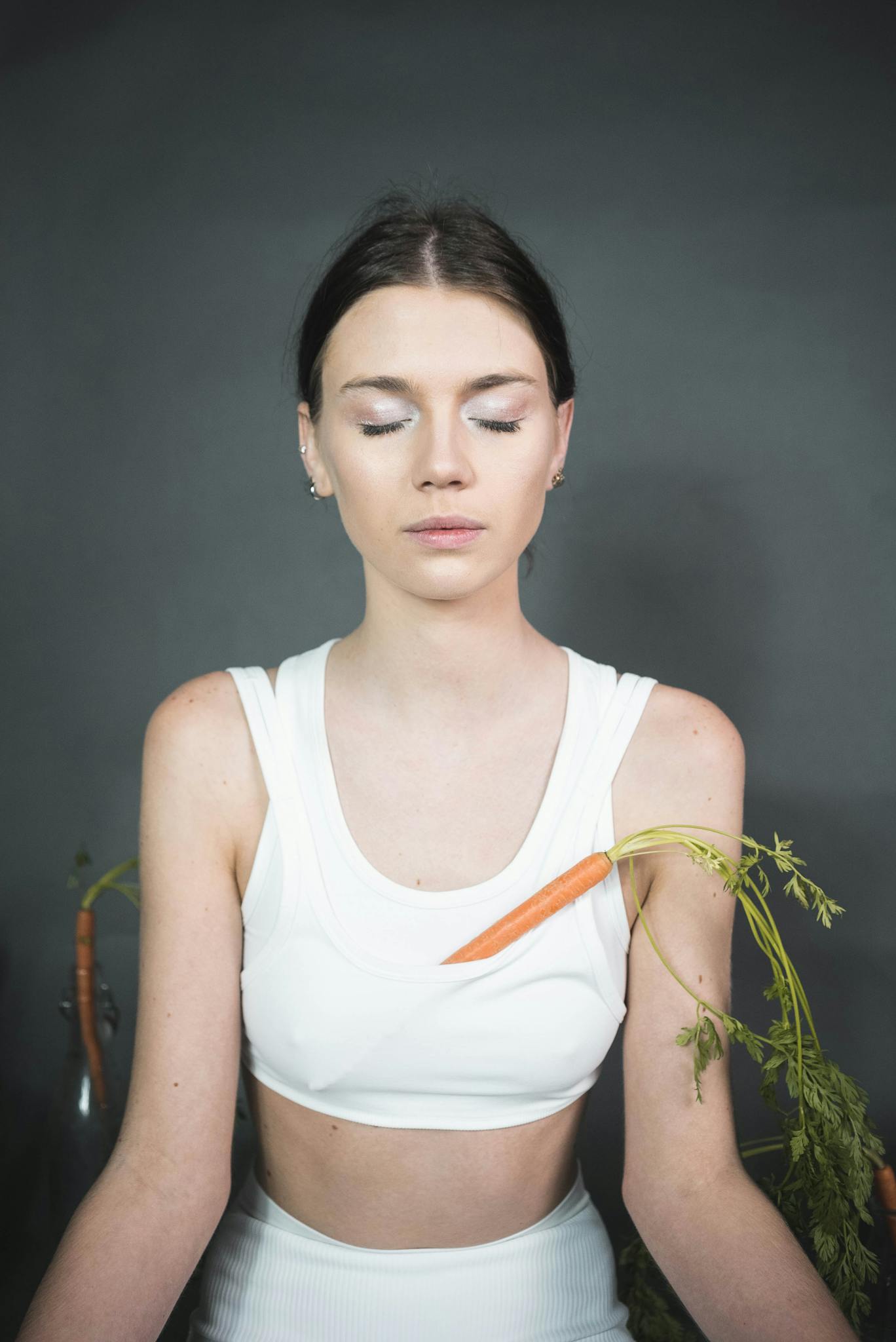 Serene woman meditating with carrot props in a studio setting.